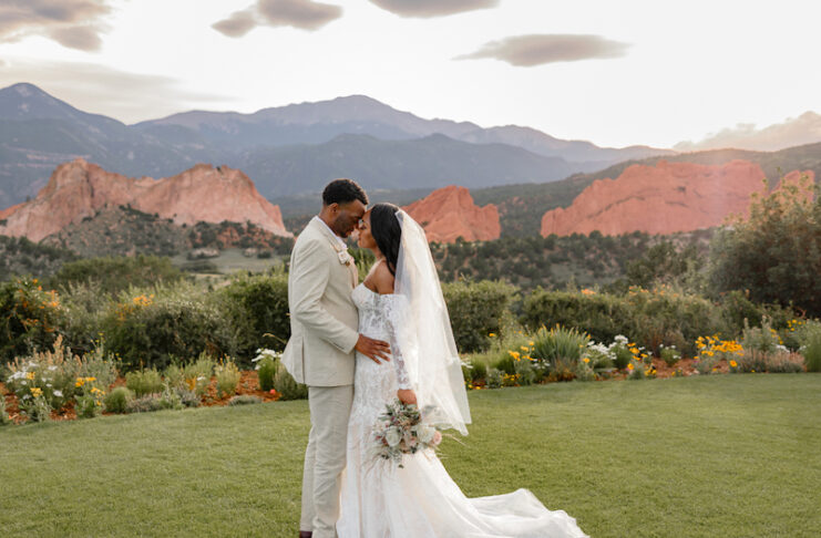 A bride and groom embrace on the lawn at Garden of the Gods Resort and Club with Pikes Peak and Garden of the Gods in the background. Photo courtesy of Garden for he Gods Resort and Club.