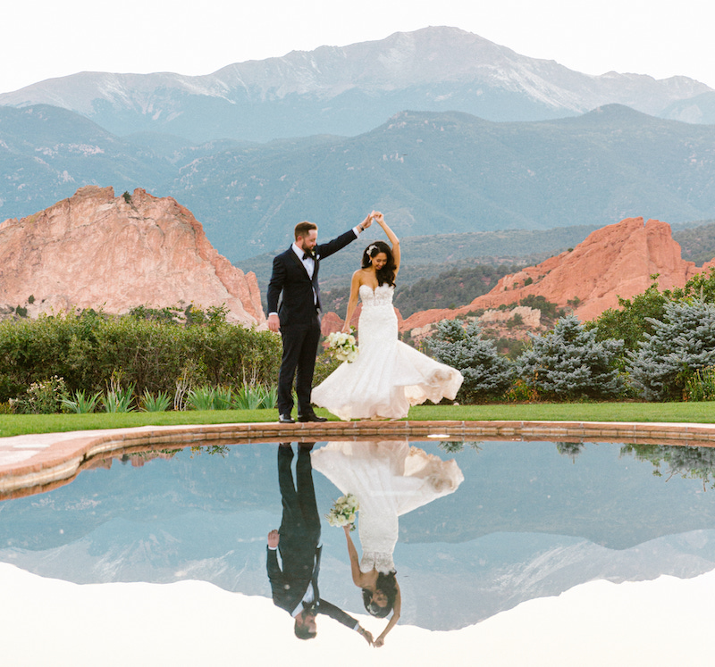 A bride and groom dance beside the reflecting pool with Garden of the Gods and Pikes Peak behind them at Garden of the Gods Resort and Club, one of the most scenic wedding venues in Colorado Springs.