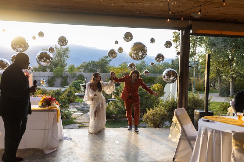 Bride and groom enter the reception where many disco balls hang from the ceiling and Pikes Peak glows on the horizon at Hillside Gardens.