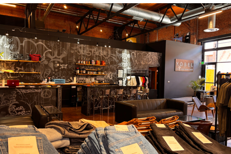 Interior view of Yobel with clothing on racks on on tables. Full bar in background.