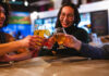 Friends cheers with beer glasses at Voodoo Brewing, enjoying cheap drinks with the Crafts and Drafts Passport in Colorado Springs.