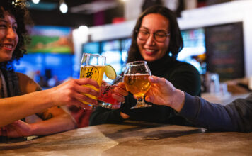 Friends cheers with beer glasses at Voodoo Brewing, enjoying cheap drinks with the Crafts and Drafts Passport in Colorado Springs.