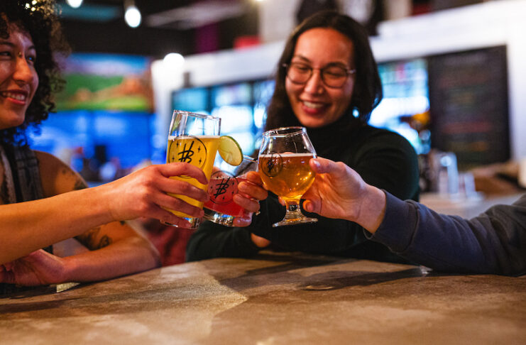 Friends cheers with beer glasses at Voodoo Brewing, enjoying cheap drinks with the Crafts and Drafts Passport in Colorado Springs.