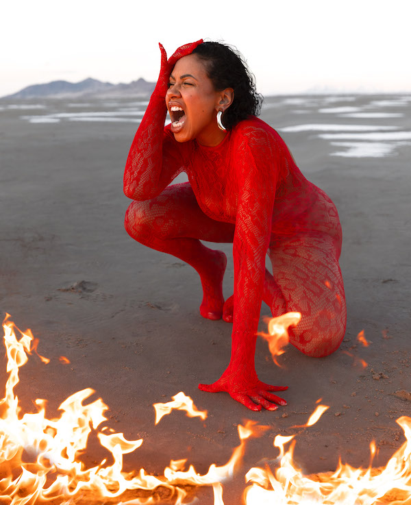 A woman in red lace holds her head and screams in the desert as flames burn at her feet in this photo by Jesus Rodriguez for the Sin art exhibition at the Bosky Studio in Colorado Springs