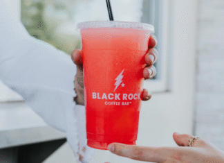 Black Rock Coffee Pink colored drink served over ice is handed to someone. Black Rock Coffee on the cup.