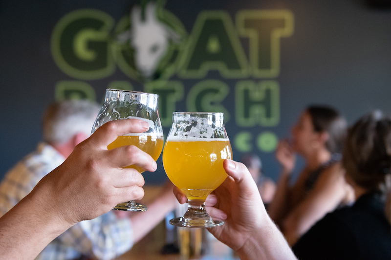 Glasses of beer clink in cheers at Goat Patch Brewing, a must-go if you're visiting Colorado Springs.