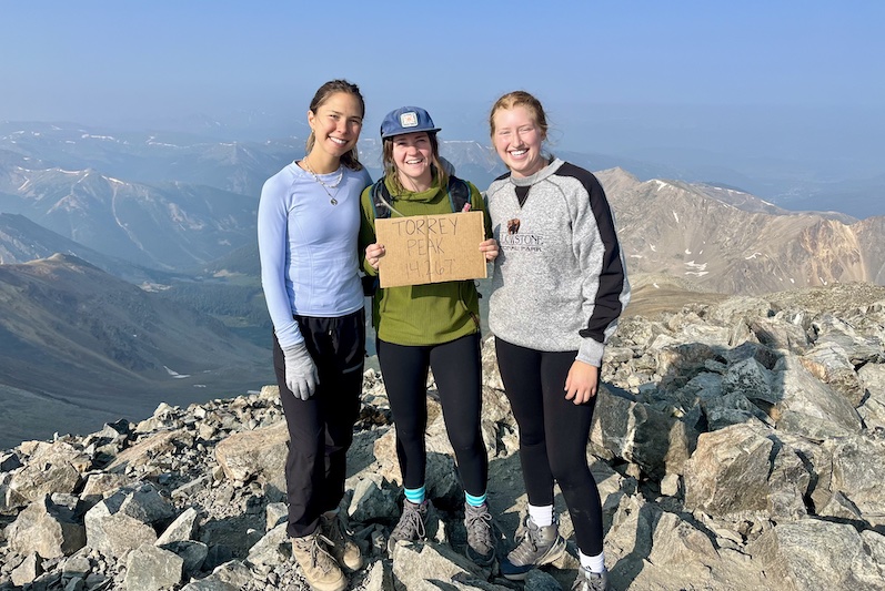 Hikers with a sign on top of Torreys Peak, a Colorado 14er near Idaho Springs