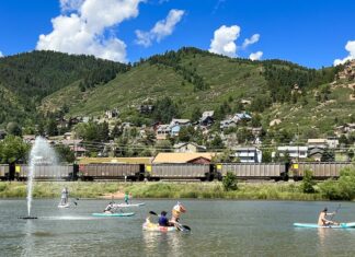 People paddle SUPs and an inflatable swan on Palmer Lake as a train passes by. Mountains line the horizon. It all makes Palmer Lake one of the best lakes in Colorado Springs.