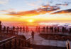 A group of people stands on the observation deck and watches sunrise on Pikes Peak.