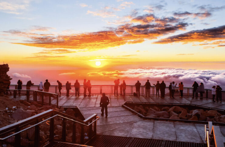 A group of people stands on the observation deck and watches sunrise on Pikes Peak.