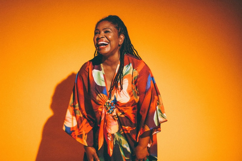 Gospel folk blues artist Ruthie Foster laughing in a colorful orange dress.