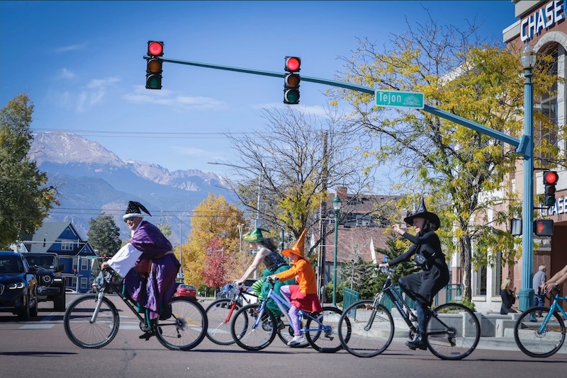 A line of bike riders in Halloween costumes ride across the street with Pikes Peak in the background on the Witches, Warlocks and Ghouls Ride, a popular fundraising ride for Halloween in Colorado Springs.