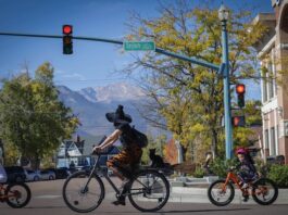 Your Ultimate Guide to Halloween in Colorado Springs A mom witch and kids in Halloween costumes ride bikes across the street with Pikes Peak in the background on the Witches, Warlocks and Ghouls Ride, a popular fundraising ride for Halloween in Colorado Springs.