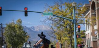 Your Ultimate Guide to Halloween in Colorado Springs A mom witch and kids in Halloween costumes ride bikes across the street with Pikes Peak in the background on the Witches, Warlocks and Ghouls Ride, a popular fundraising ride for Halloween in Colorado Springs.