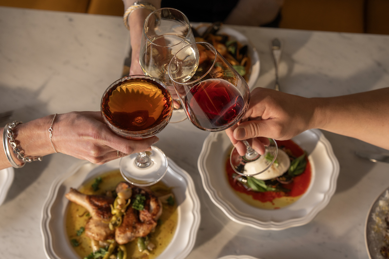 Cheers with wine glasses over a table of Italian dishes at Oro during its special Thanksgiving meals.