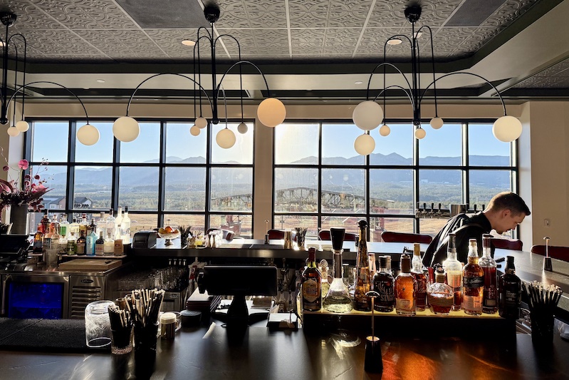 Golden hour sunlight shines over the Front Range mountains into Brohan's, the upstairs cocktail bar at Roth's Sea and Steak at Ford Amphitheater in Colorado Springs