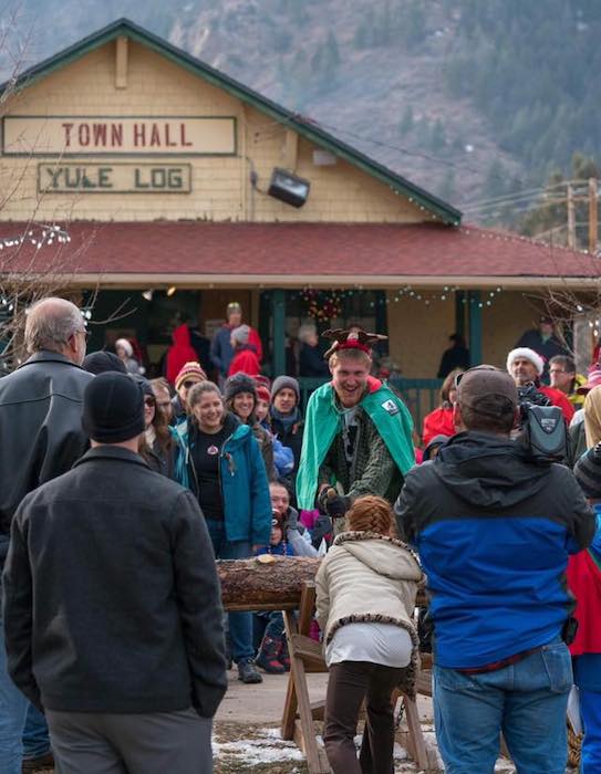 A young girl and log cutter use a two-handled saw to cut the Palmer Lake Yule Log in 2017.
