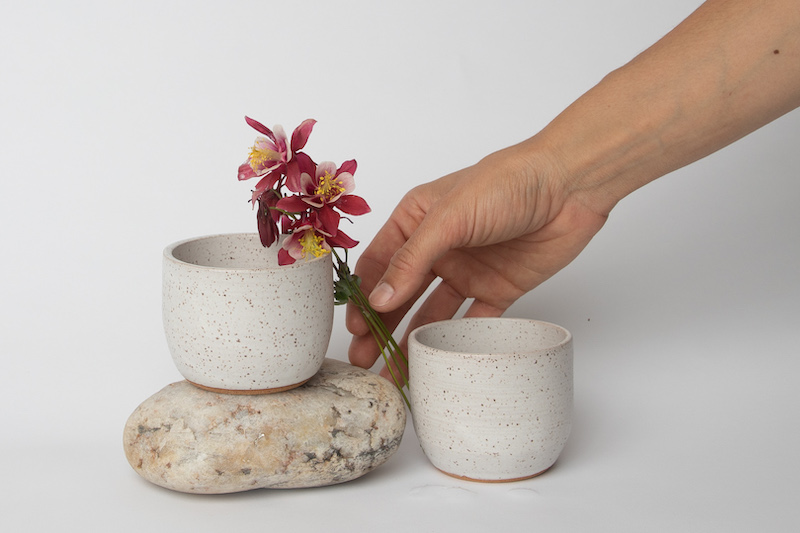 A hand places flowers beside ceramic mugs made at Ink and Mud Co where you can find Colorado Springs arts classes in pottery and ceramics.