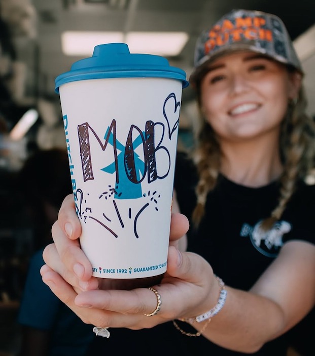 A Dutch Bros barista offers a cup of coffee through the drive-thru window.