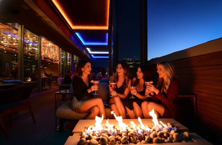 A group of women sip cocktails by a fire pit for Galentine's Day at rooftop Ryze Skyline Lounge.