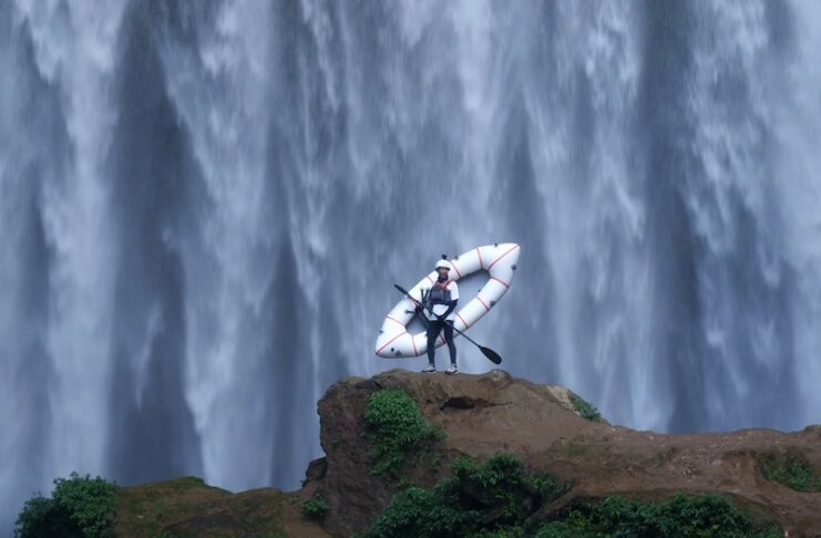 A kayaker stands in front of a massive waterfall in an image for the Paddling Film Festival, one of the best things to do in Colorado Springs this weekend.
