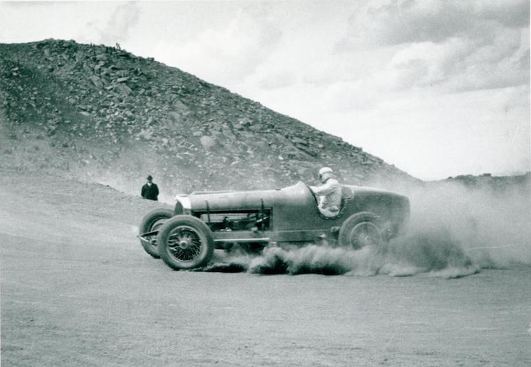 A historical open wheel race car driven by Chuck Myers throws gravel around a corner in the Pikes Peak Hill Climb.
