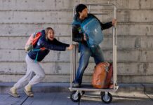 A girl pushes a guy on a luggage cart while wearing Cotopaxi Allpa Travel Packs