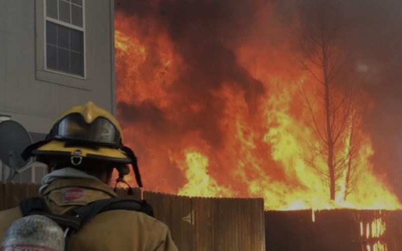 A firefighter battles a wildfire to protect a home