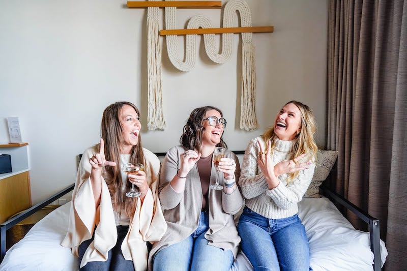 Three women laugh inside a room at Kinship Landing hotel in Colorado Springs