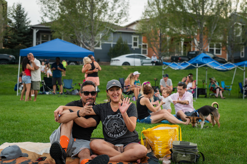 A couple sitting on a blanket wave at Music on the Mesa at Gold Hill Mesa