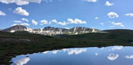 The Best Mountain Passes in Southern Colorado Peaks and clouds reflected in a lake at the summit of Independence Pass, one of the most scenic drives in Colorado.