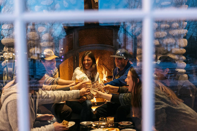 Friends laugh beside the river rock fireplace in Surf Hotel