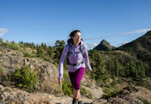 A woman hikes in the mountains wearing an Icebreaker Quantum Hoodie, one of our favorite hiking gear picks.