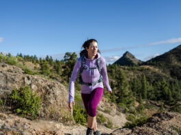 Our Favorite Hiking Gear Now A woman hikes in the mountains wearing an Icebreaker Quantum Hoodie, one of our favorite hiking gear picks.