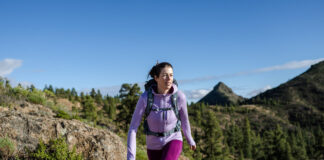 Our Favorite Hiking Gear Now A woman hikes in the mountains wearing an Icebreaker Quantum Hoodie, one of our favorite hiking gear picks.