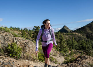 Our Favorite Hiking Gear Now A woman hikes in the mountains wearing an Icebreaker Quantum Hoodie, one of our favorite hiking gear picks.