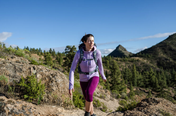 A woman hikes in the mountains wearing an Icebreaker Quantum Hoodie, one of our favorite hiking gear picks.
