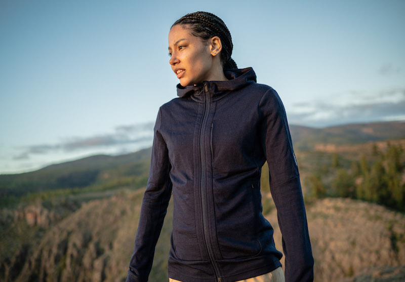 A woman in the mountains wearing a merino wool Icebreaker Quantum III full zip hoodie.